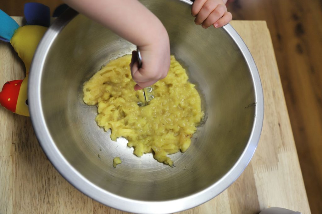 toddler mashing bananas for banana muffins